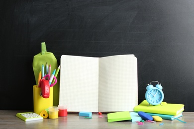 Photo of Different school stationery and blank notebook on table near chalkboard. Space for text