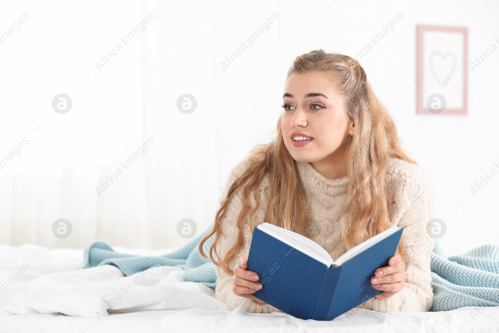 Photo of Attractive young woman in cozy warm sweater reading book on bed at home. Space for text