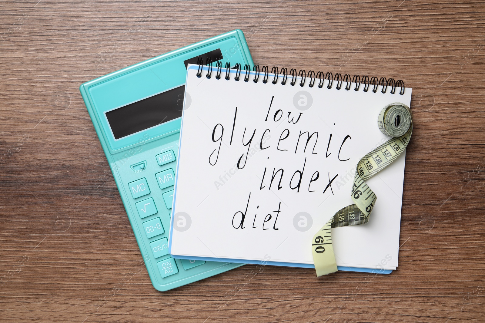 Photo of Notebook with words Low Glycemic Index Diet, measuring tape and calculator on wooden table, flat lay