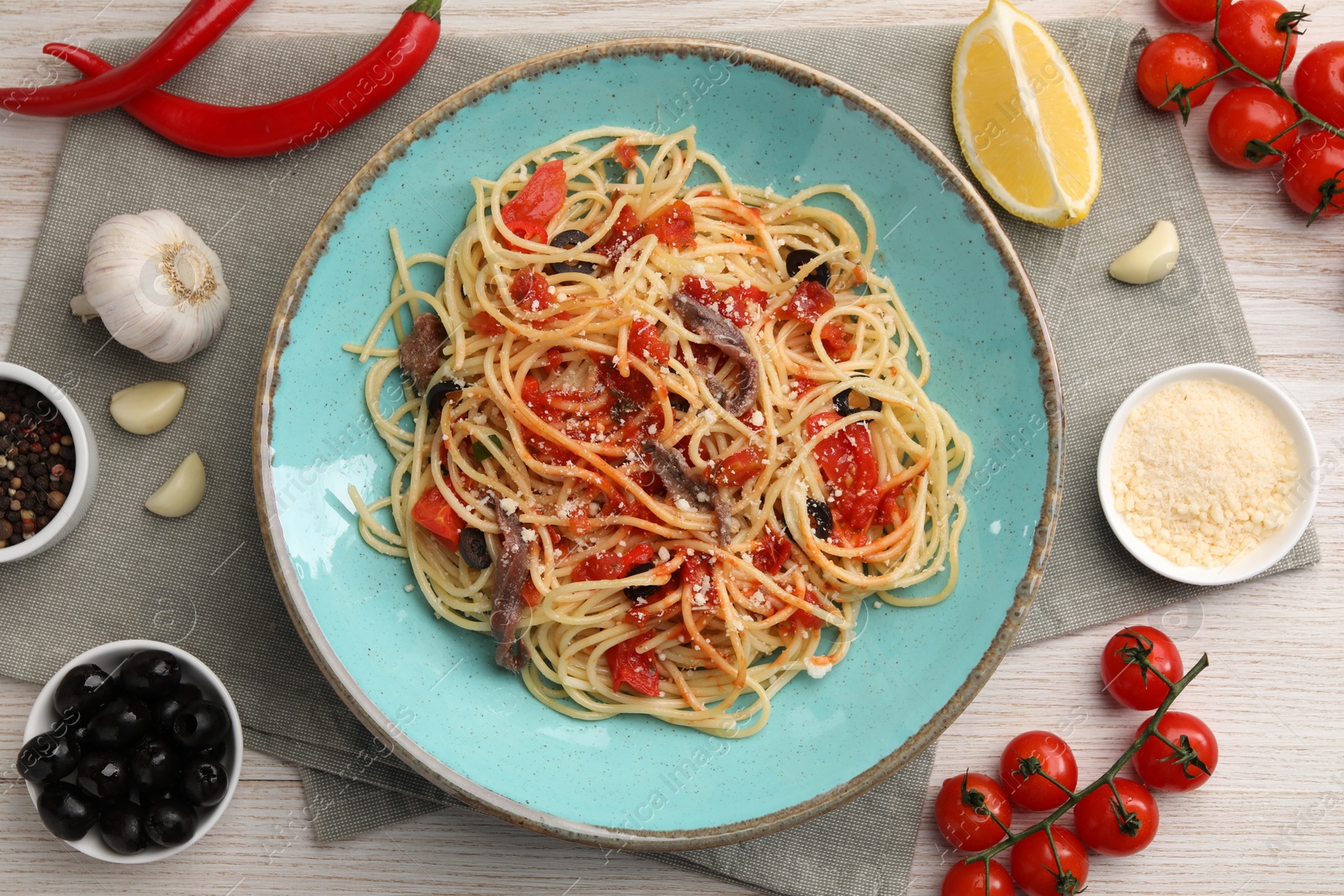 Photo of Plate of delicious pasta with anchovies, tomatoes and parmesan cheese near ingredients on white wooden table, flat lay