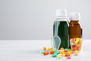 Bottles of syrups with pills on wooden table against white background, space for text. Cough and cold medicine