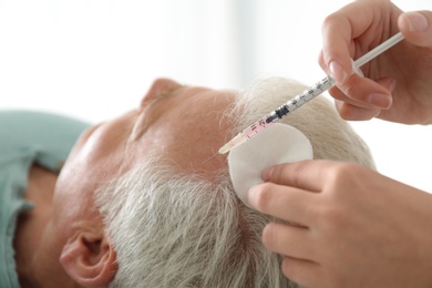 Photo of Senior man with hair loss problem receiving injection in salon, closeup