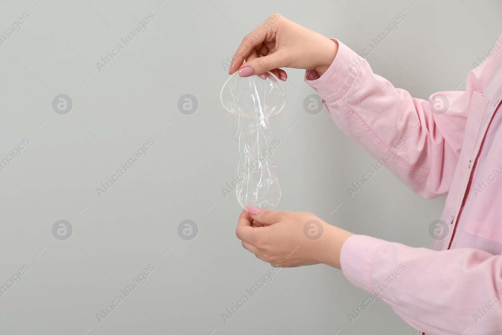 Photo of Woman with unrolled female condom on light grey background, closeup. Space for text