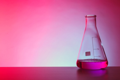 Conical flask with liquid on table against color background. Chemistry laboratory glassware