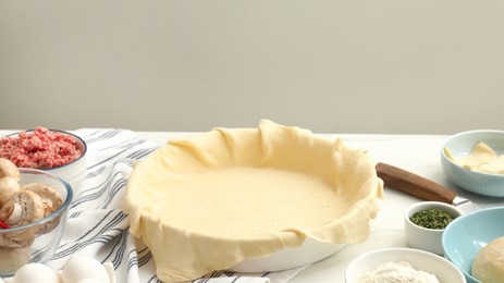 Raw dough and ingredients for meat pie on white table, space for text.