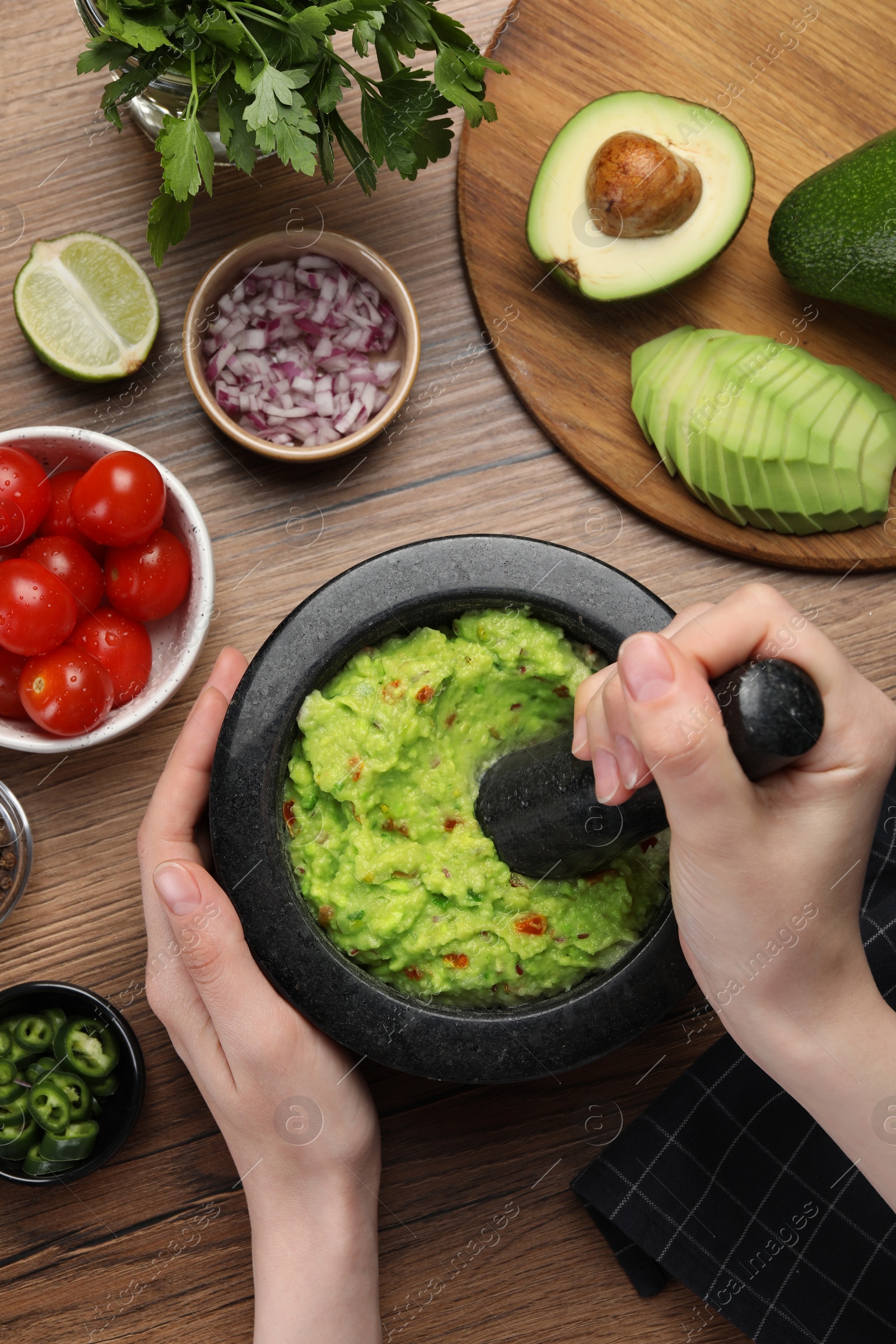 Photo of Woman preparing delicious guacamole at wooden table, top view