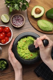 Woman preparing delicious guacamole at wooden table, top view