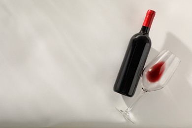 Photo of Bottle of expensive red wine and wineglass on light grey background, top view. Space for text