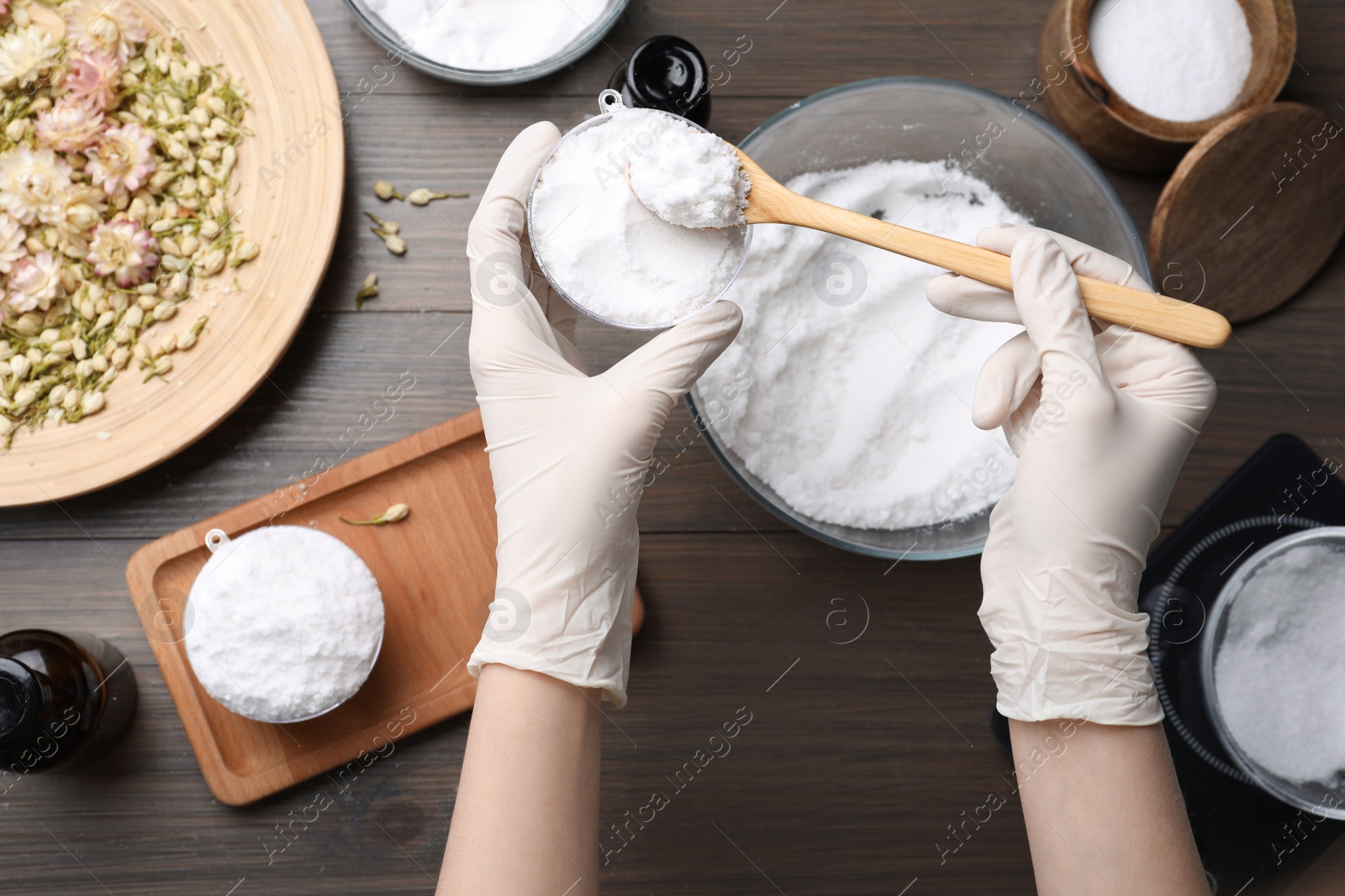 Photo of Woman in gloves making bath bomb at wooden table, top view