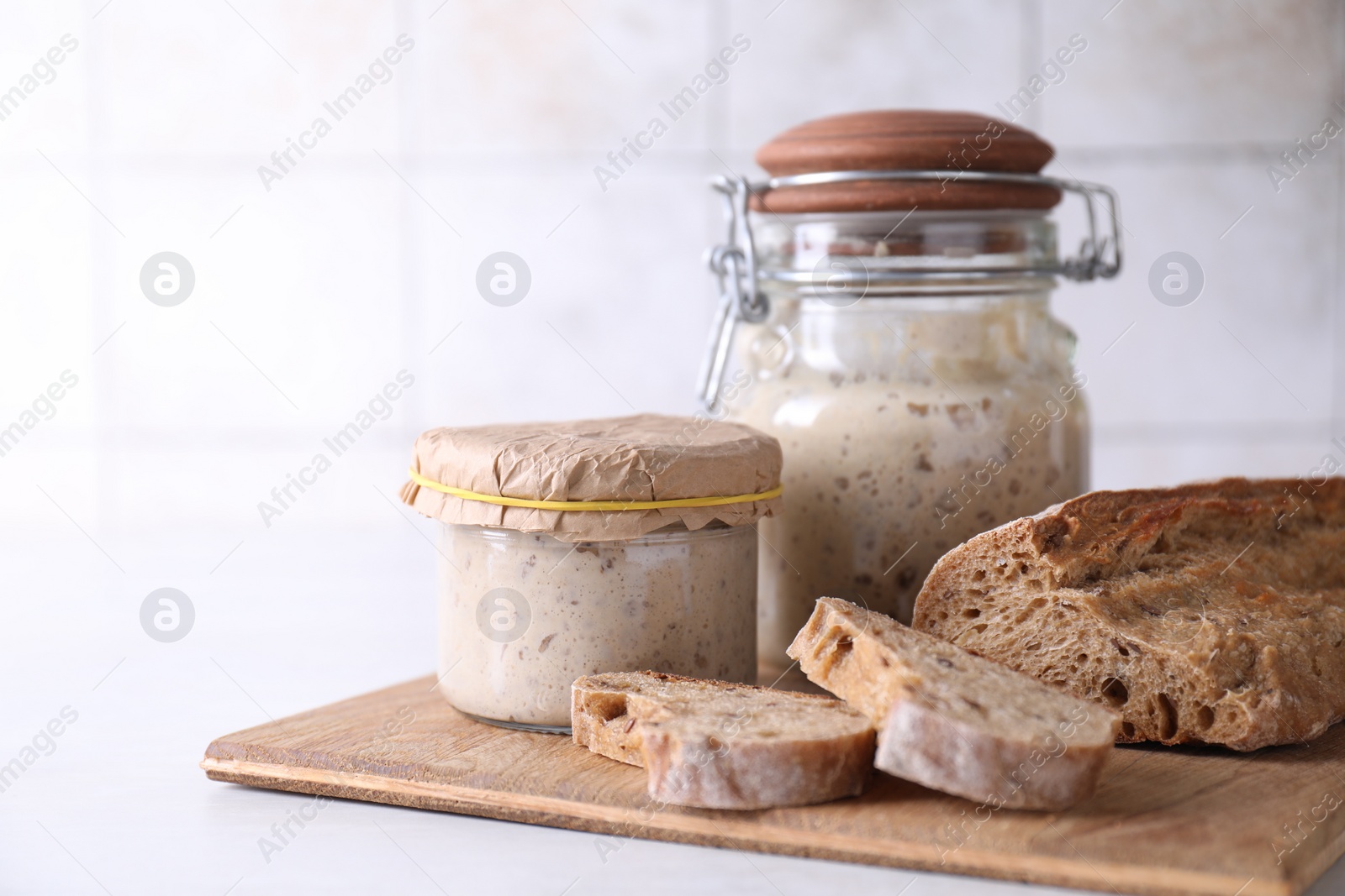 Photo of Sourdough starter in glass jars and fresh bread on light table. Space for text