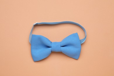 Photo of Stylish light blue bow tie on pale orange background, top view