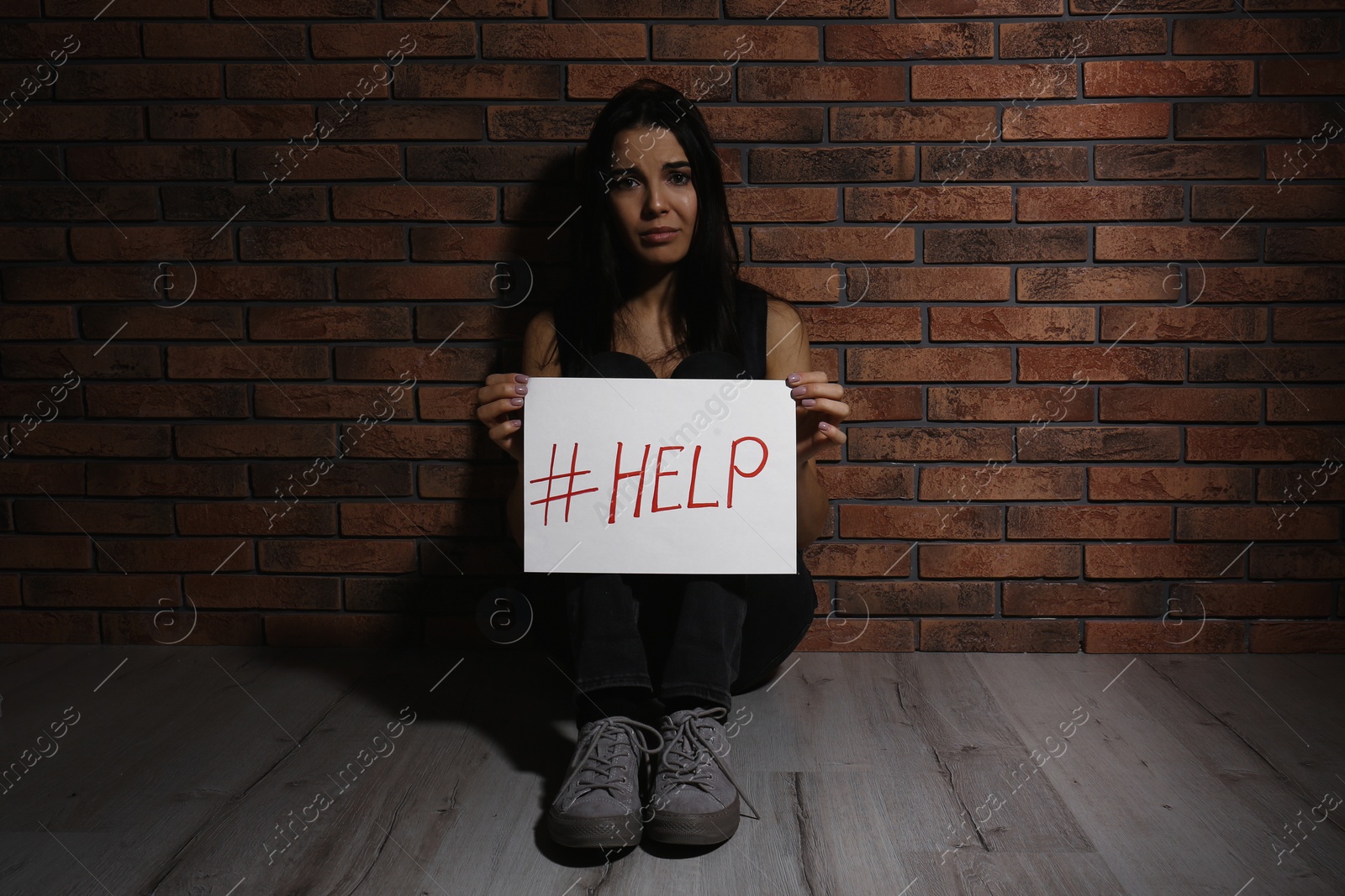 Photo of Abused young woman with hashtag HELP near brick wall. Domestic violence concept