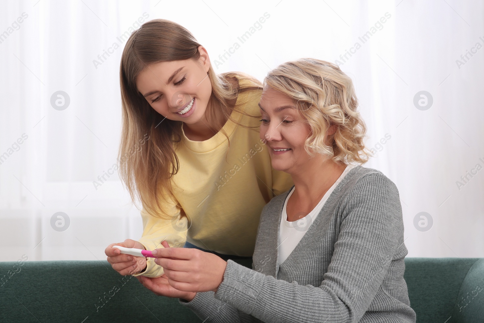 Photo of Young woman showing her mother pregnancy test at home. Grandparent reaction to future grandson