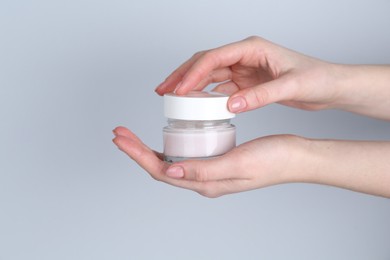 Woman holding jar of cream on grey background, closeup