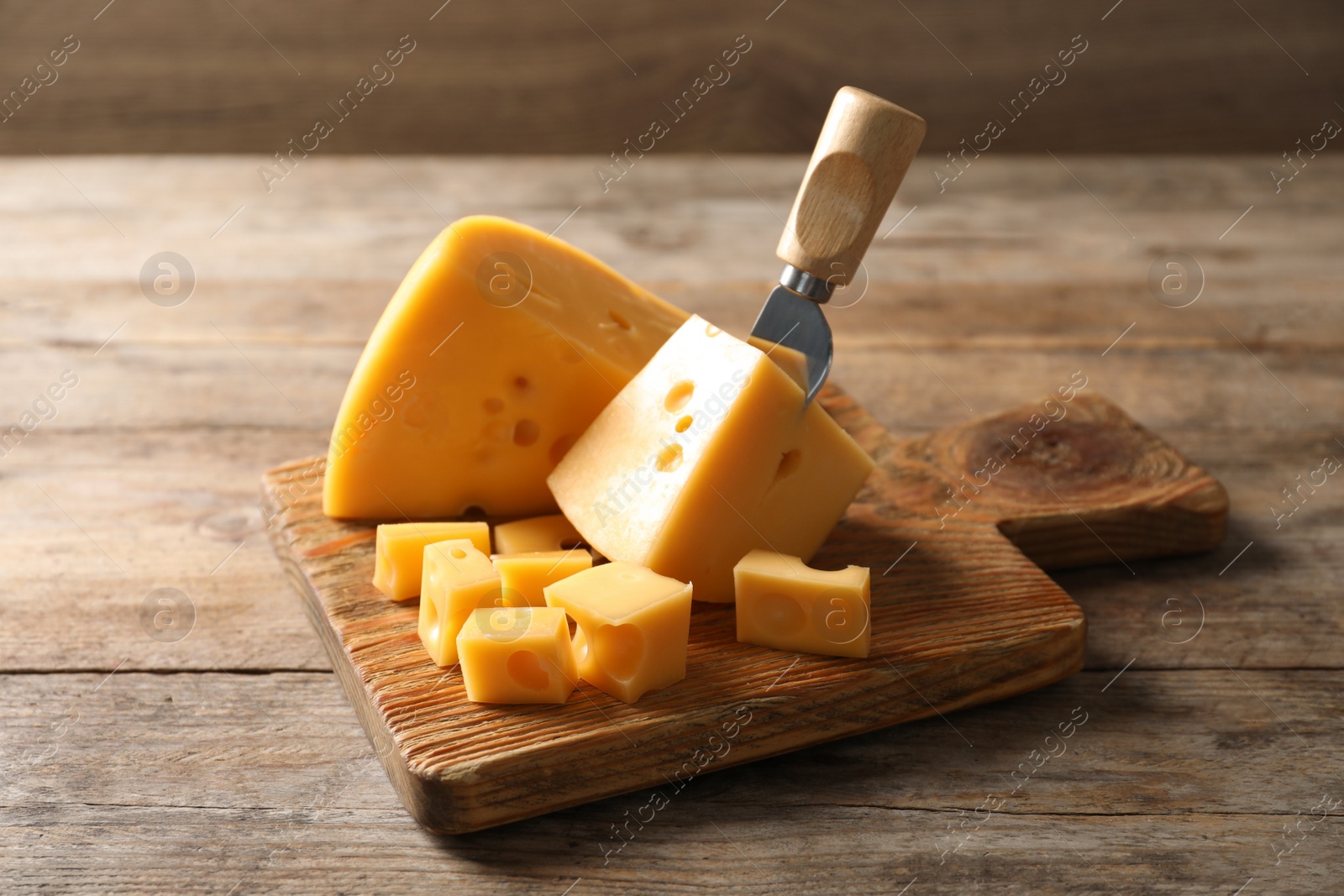 Photo of Serving board with delicious cheese on wooden table