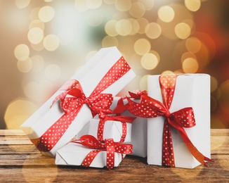 Image of Christmas gift boxes on wooden table against blurred background, bokeh effect