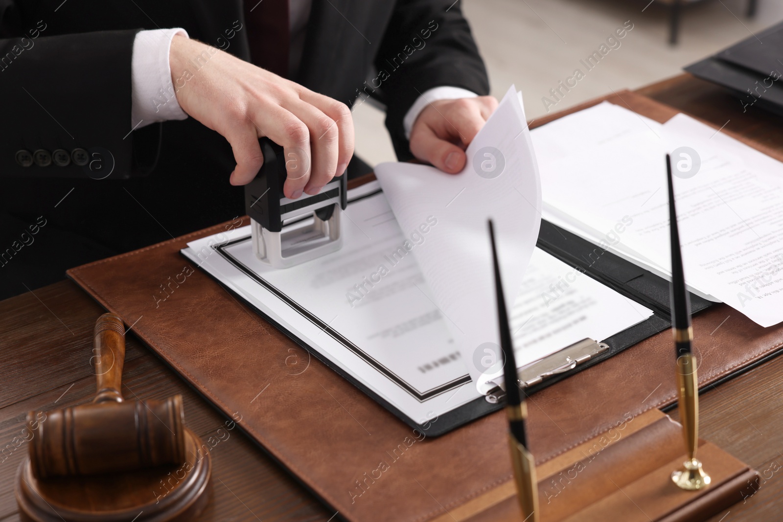 Photo of Notary stamping document at wooden table in office, closeup