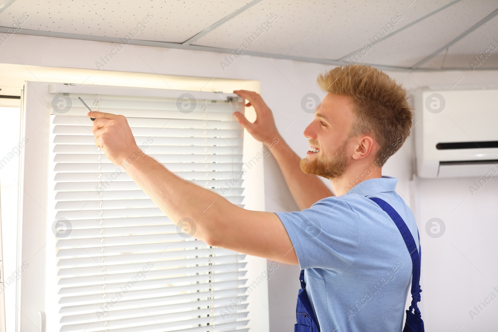 Image of Handyman with screwdriver installing window blinds indoors
