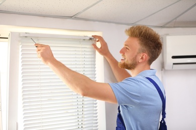 Image of Handyman with screwdriver installing window blinds indoors