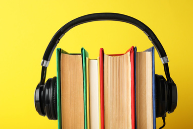 Photo of Books with modern headphones on yellow background, closeup