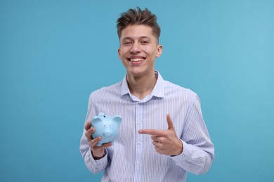 Photo of Happy man pointing at piggy bank on light blue background