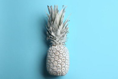 Painted white pineapple on light blue background, top view. Creative concept