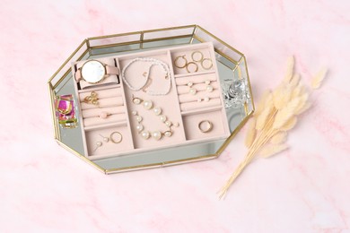 Photo of Jewelry box with many different accessories, perfumes and dry flowers on pink marble table, flat lay