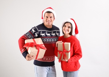 Photo of Beautiful happy couple in Santa hats holding Christmas gifts on light background