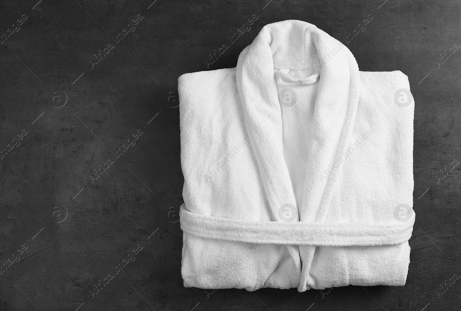 Photo of Clean folded bathrobe on black stone background, top view