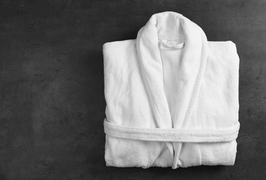 Photo of Clean folded bathrobe on black stone background, top view