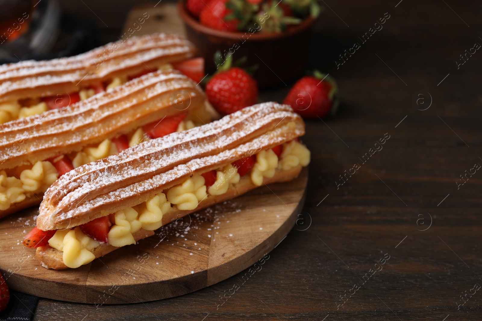 Photo of Delicious eclairs filled with cream and strawberries on wooden table, space for text