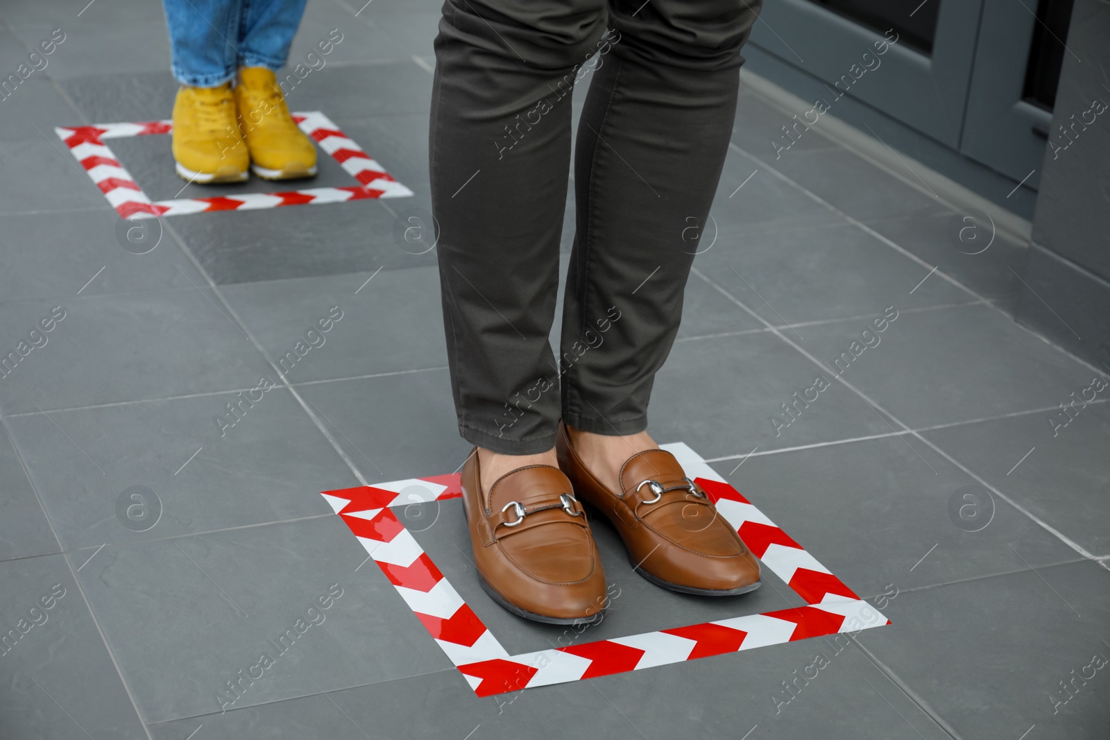 Photo of People standing on taped floor markings for social distance, closeup. Coronavirus pandemic