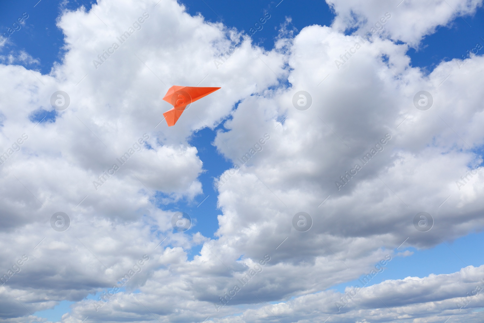 Image of Orange paper plane flying in blue sky with clouds