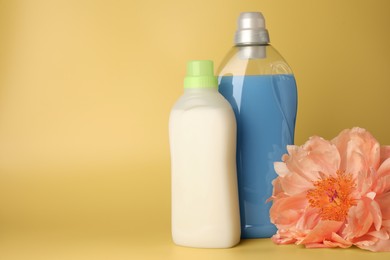 Photo of Bottles of fabric softener and beautiful flower on pale yellow background, space for text