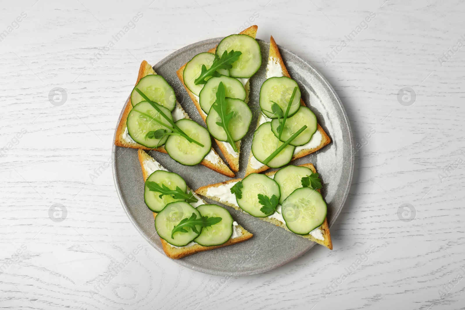 Photo of Plate with traditional English cucumber sandwiches on white wooden background, top view