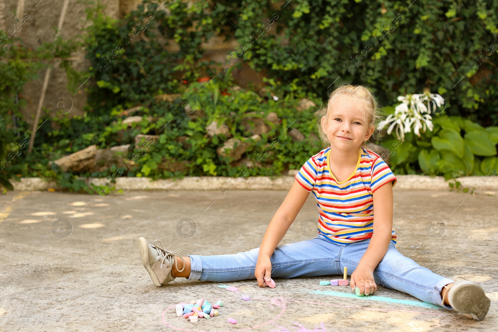 Photo of Cute little left-handed girl drawing with chalk on asphalt