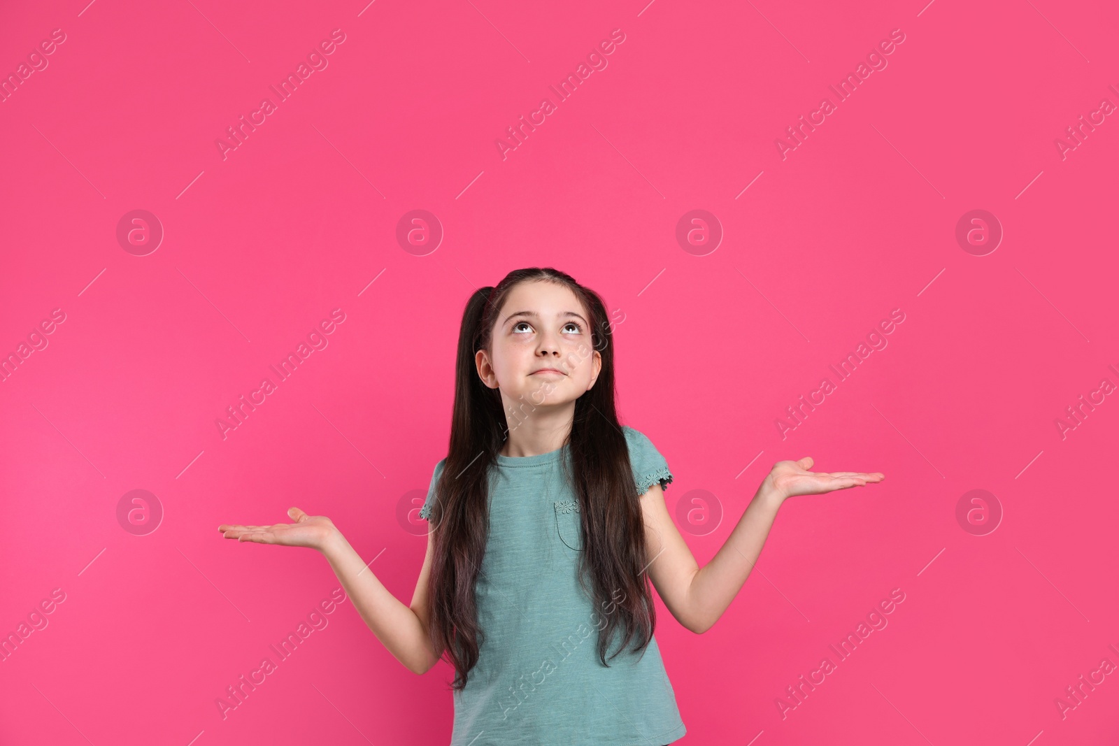 Photo of Portrait of confused little girl on pink background. Thinking about answer for question