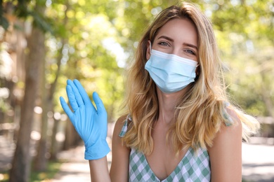 Woman in protective face mask showing hello gesture outdoors. Keeping social distance during coronavirus pandemic