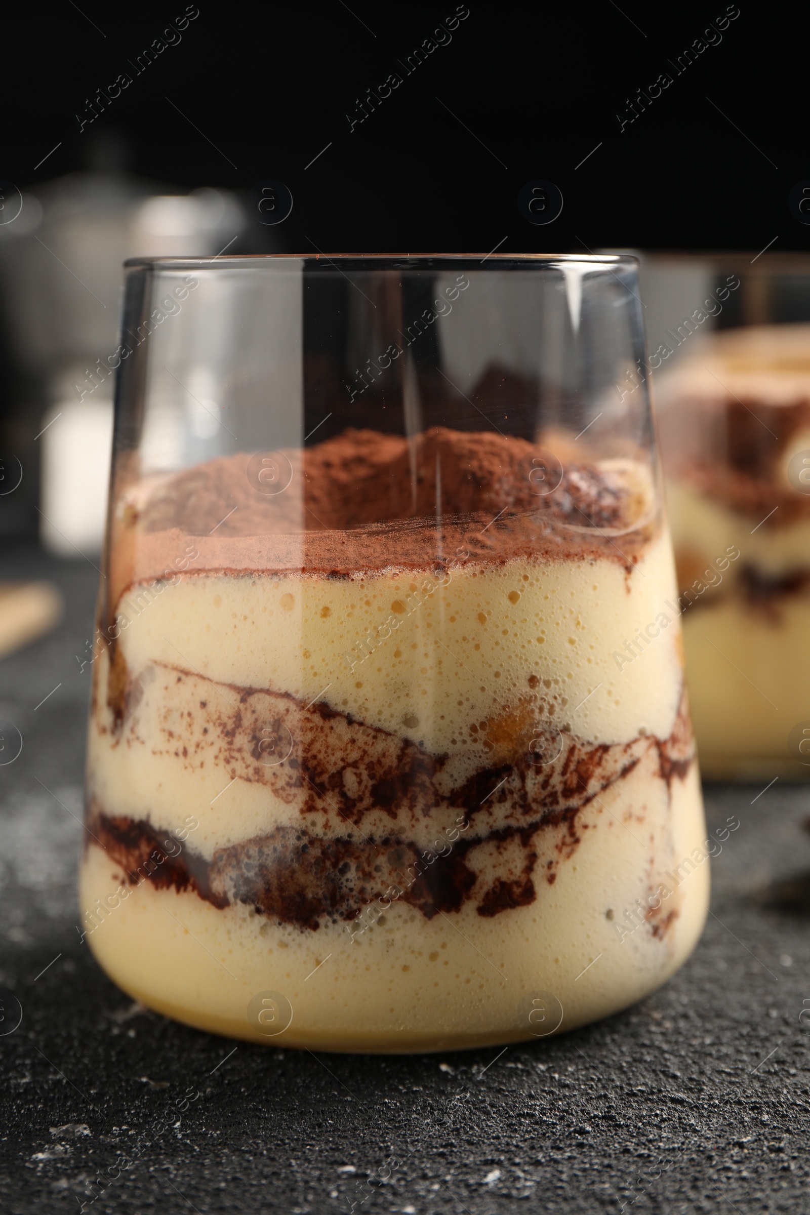 Photo of Delicious tiramisu in glass on grey textured table, closeup