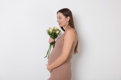 Photo of Beautiful pregnant woman in beige dress with bouquet of roses on white background