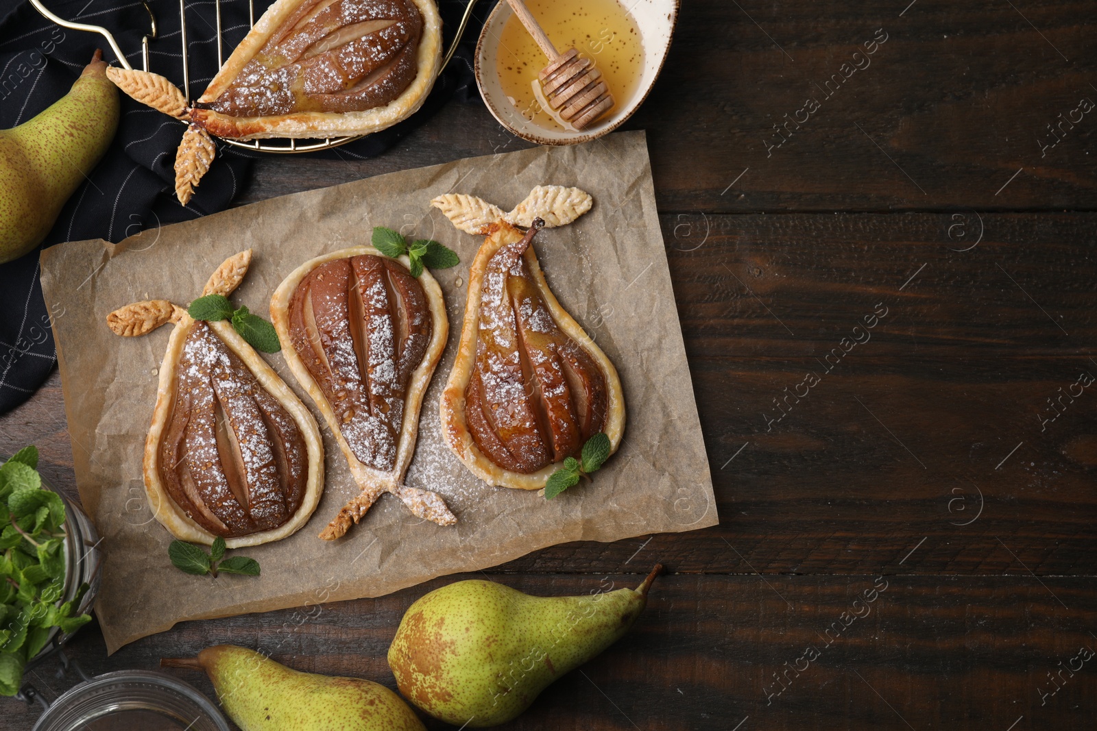 Photo of Delicious pears baked in puff pastry with powdered sugar served on wooden table, flat lay. Space for text