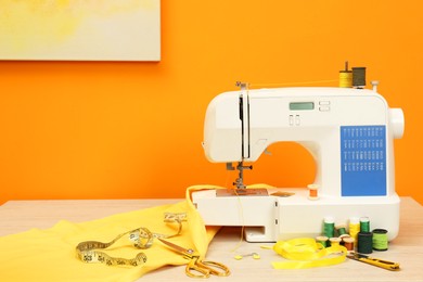 Photo of Modern sewing machine with cloth and craft accessories on wooden table near orange wall