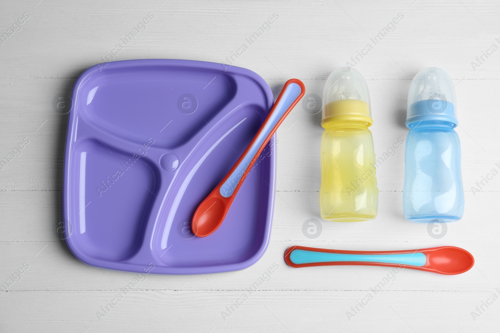 Photo of Set of colorful plastic dishware on white wooden table, flat lay. Serving baby food