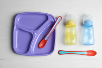 Photo of Set of colorful plastic dishware on white wooden table, flat lay. Serving baby food