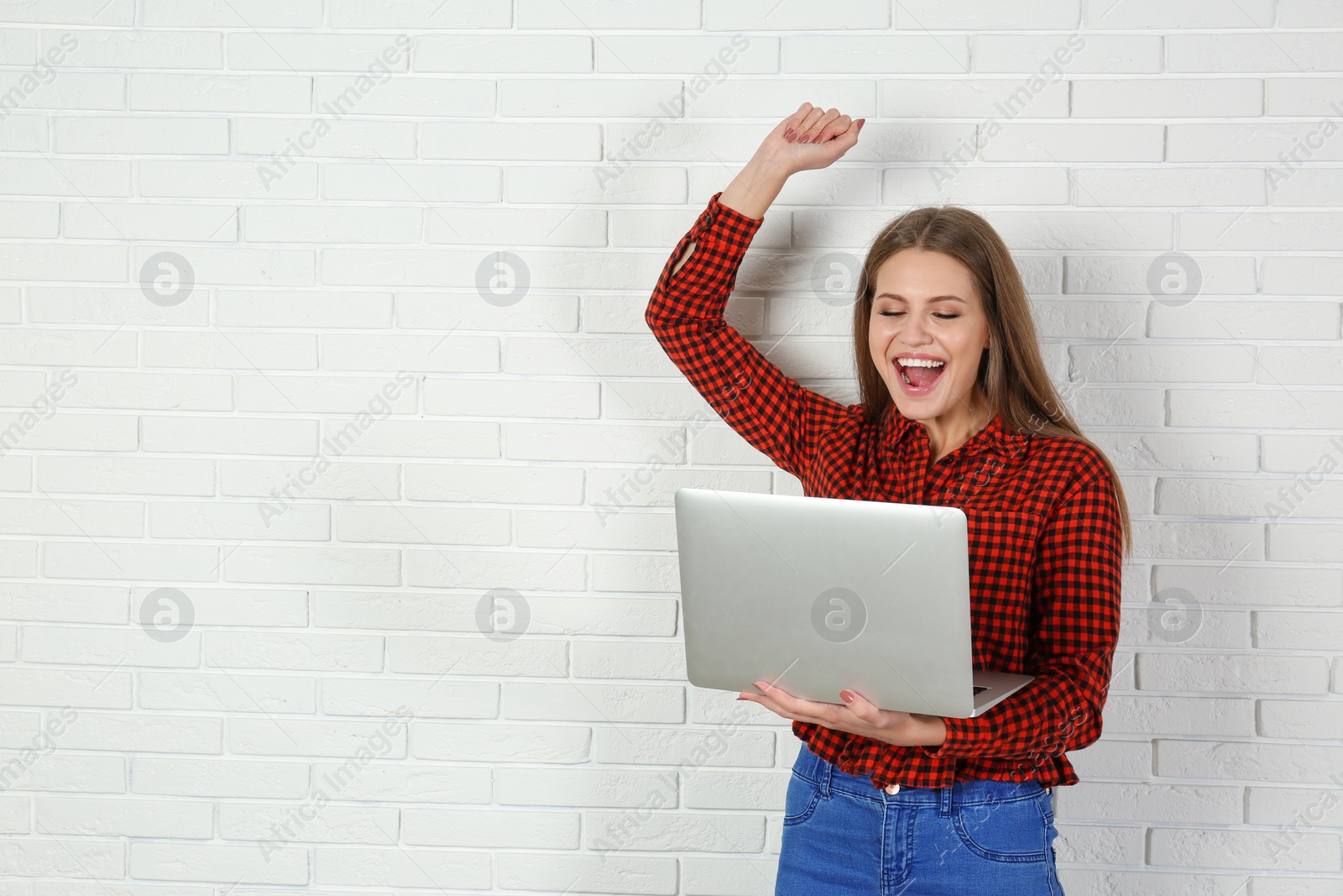 Photo of Emotional young woman with laptop celebrating victory near brick wall. Space for text