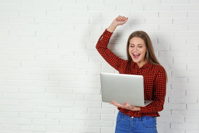 Photo of Emotional young woman with laptop celebrating victory near brick wall. Space for text