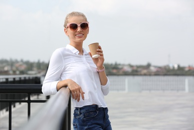 Photo of Young woman with cup of coffee standing at pier. Joy in moment