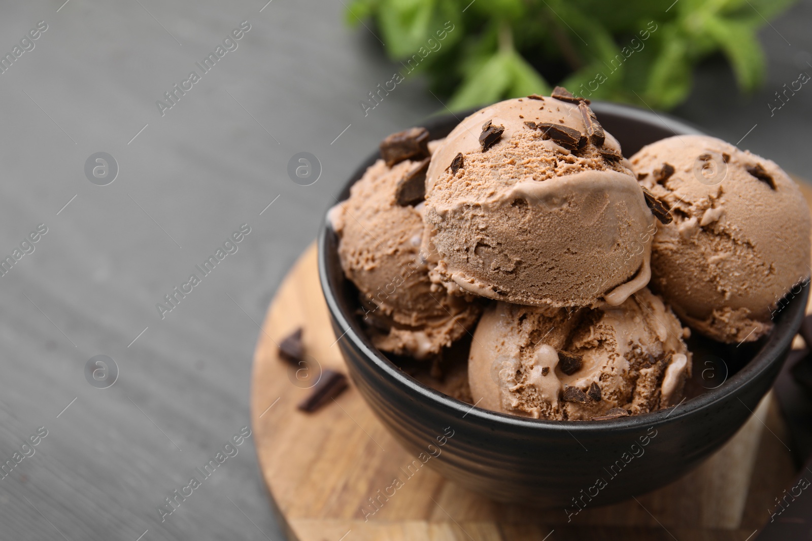 Photo of Bowl with tasty chocolate ice cream on grey wooden table, closeup. Space for text