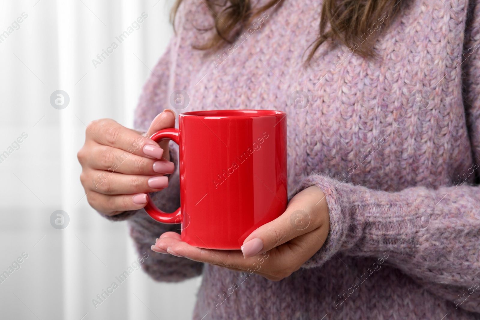 Photo of Woman holding red mug indoors, closeup. Mockup for design