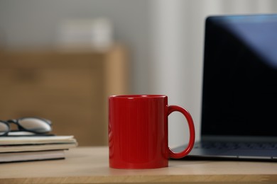 Red ceramic mug, notebooks and laptop on wooden table at workplace